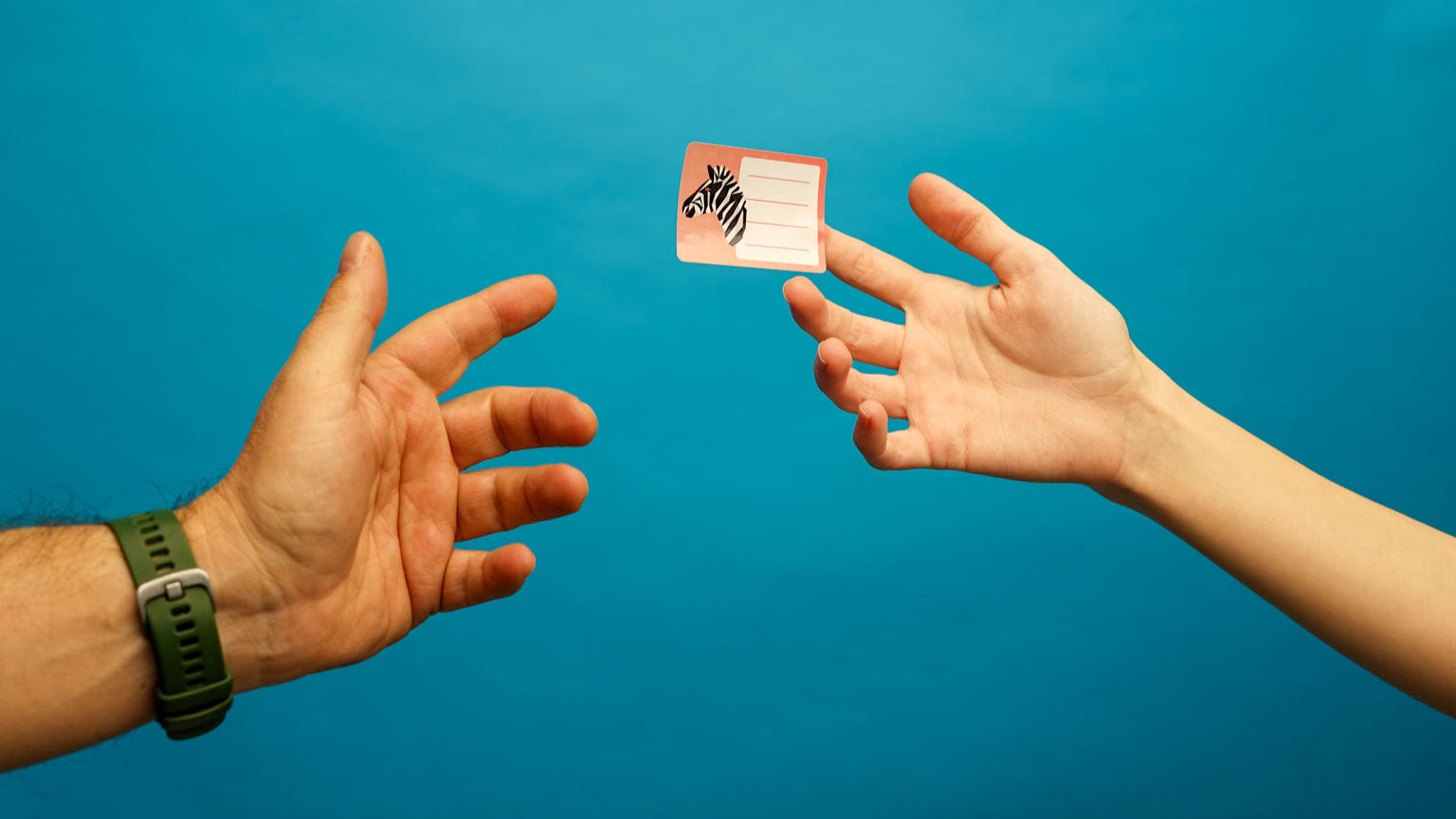 Two hands reaching towards a floating rectangular sticker with a zebra head illustration and blank lines for writing, set against a vibrant blue background. Ideal for showcasing fun and customizable name tags or labels.