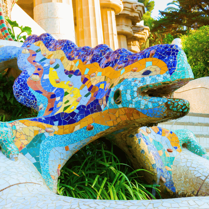 Close-up of a colorful mosaic dragon sculpture, likely a famous landmark, adorned with vibrant blue, yellow, and orange ceramic tiles, with lush green foliage in the foreground. Ideal for promoting travel or art-related products.